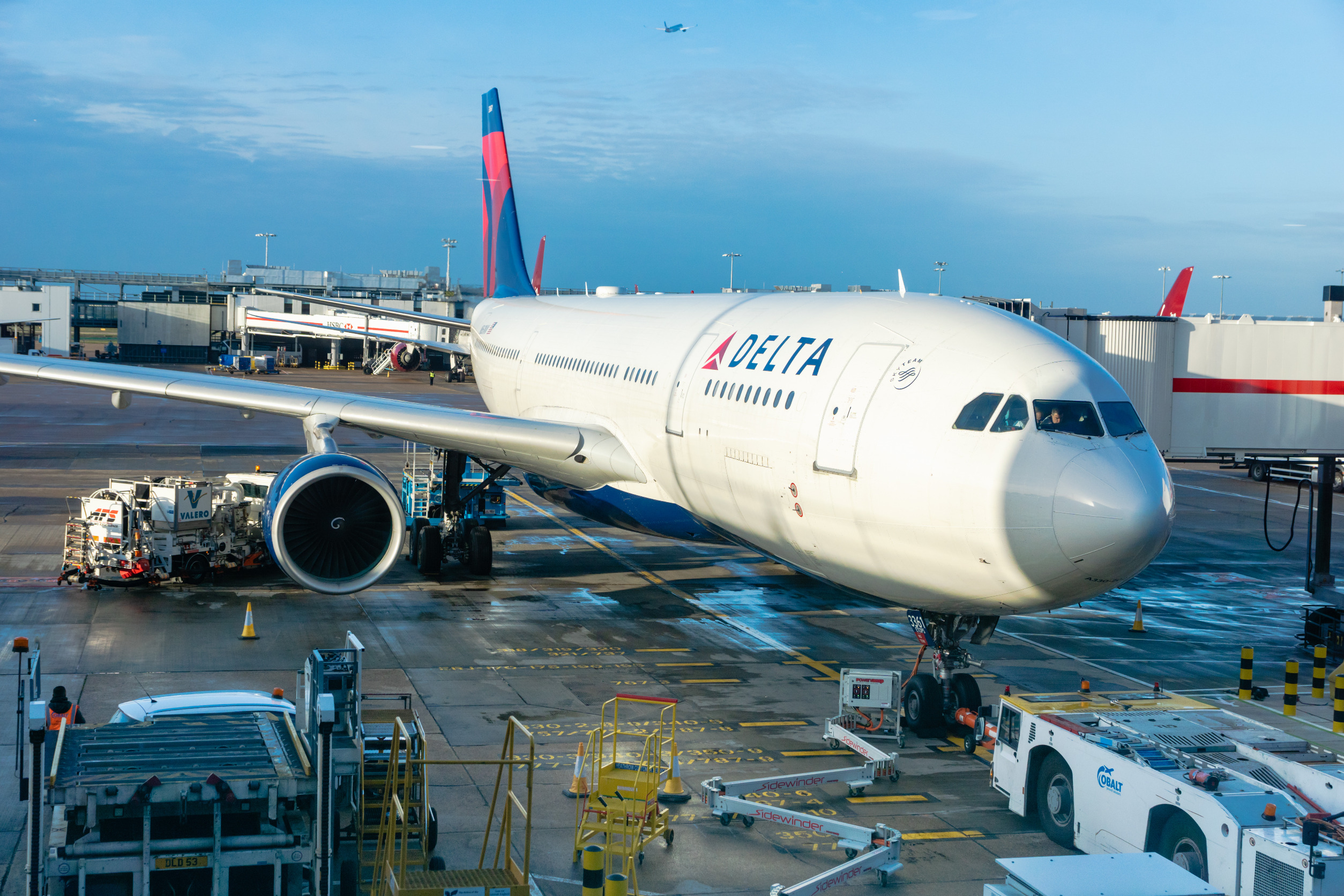 Delta Air Lines passenger aircraft parked at an airport gate while ground crews prepare the plane for departure.