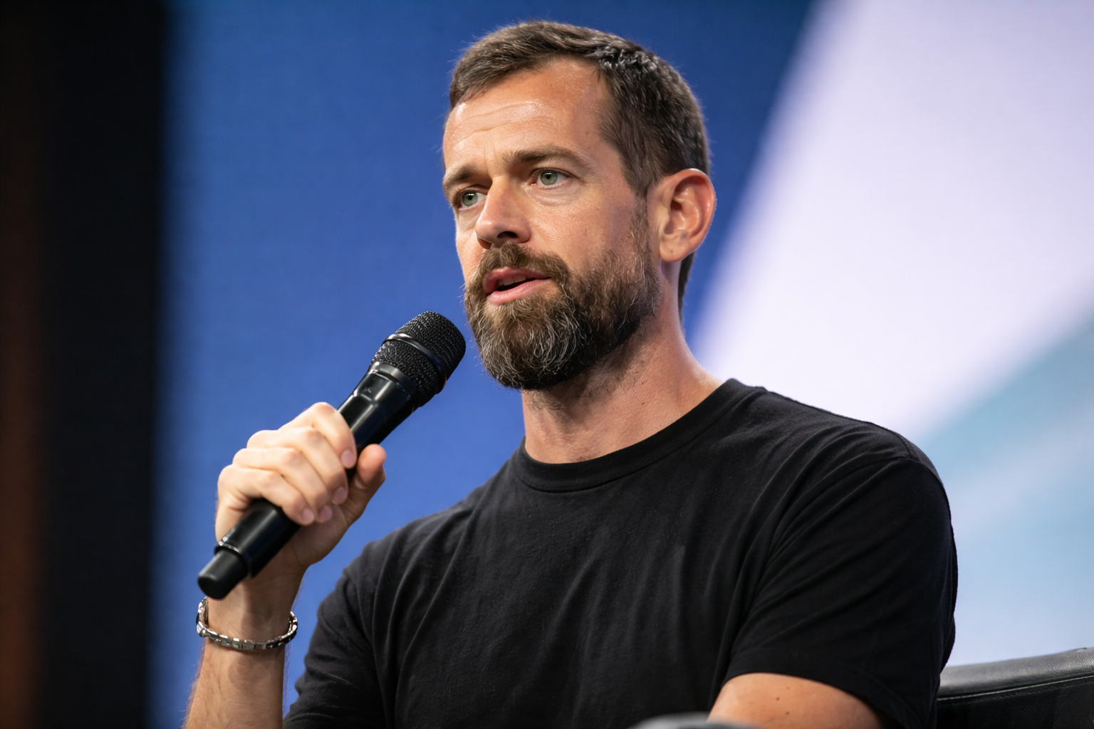 Jack Dorsey speaking into a handheld microphone on stage during a conference panel discussion.