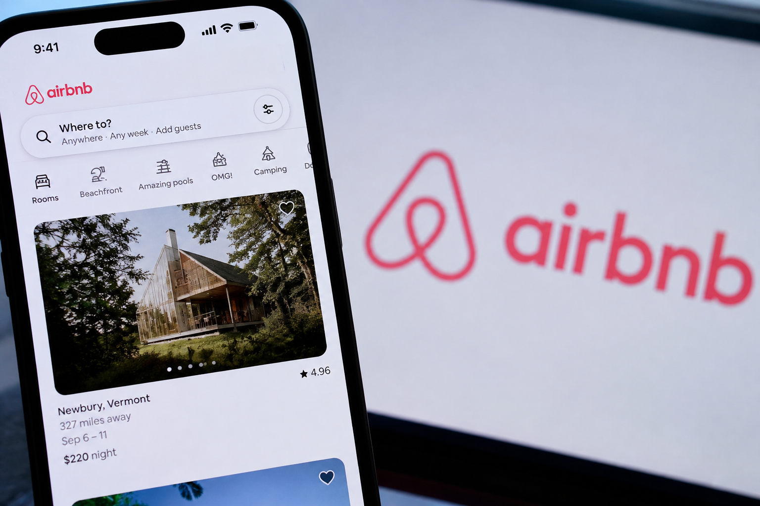 Airbnb-App auf einem Smartphone; das Firmenlogo ist auf einem Bildschirm im Hintergrund sichtbar.